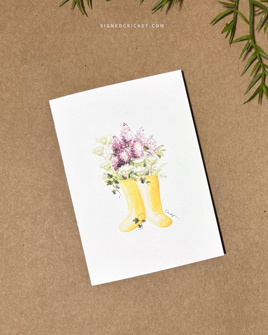 5x7 greeting card featuring watercolor illustration of yellow boots, purple liliacs, white and green Queen Anne's lace, and dark green English ivy