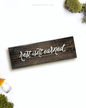 Dark brown wooden sign with 'rest isn't earned' text written on it, lying on a white background