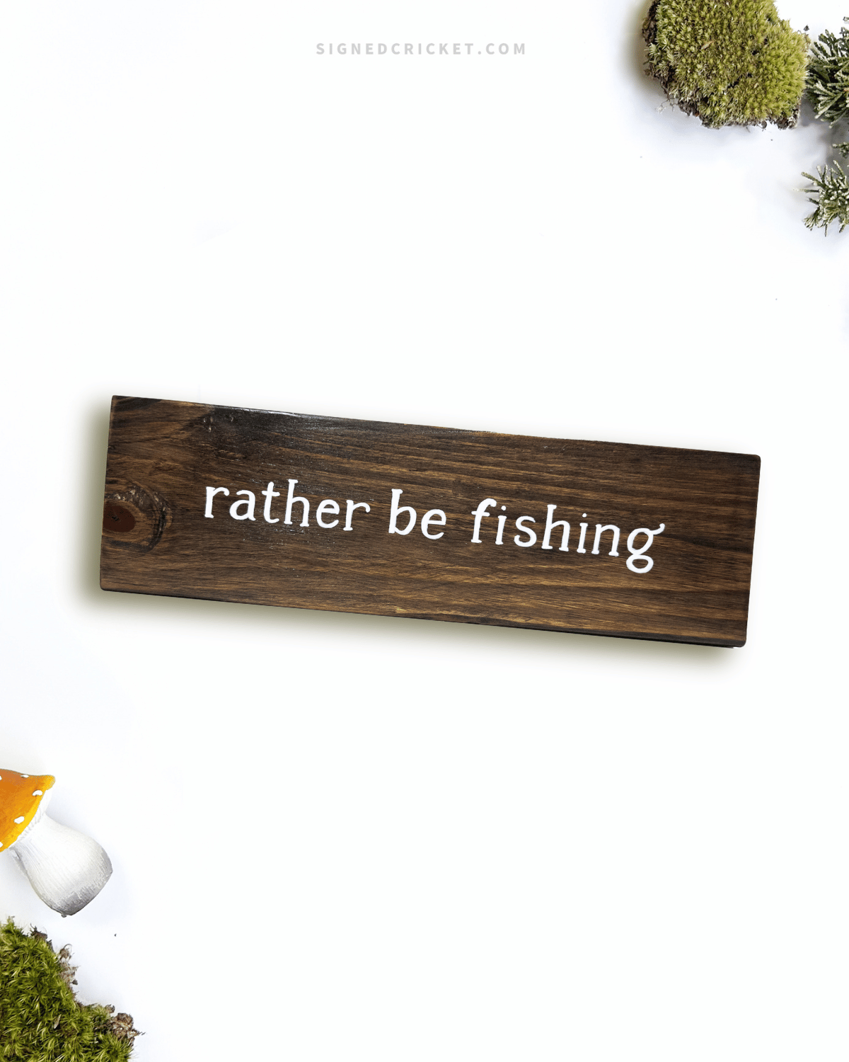 Dark brown wooden sign with 'rather be fishing' text written on it, lying on a white background