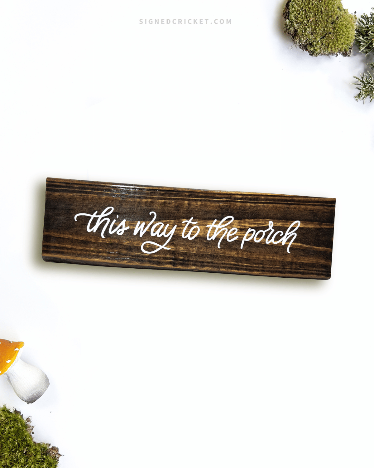 Dark brown wooden sign with 'this way to the porch' text written on it, lying on a white background