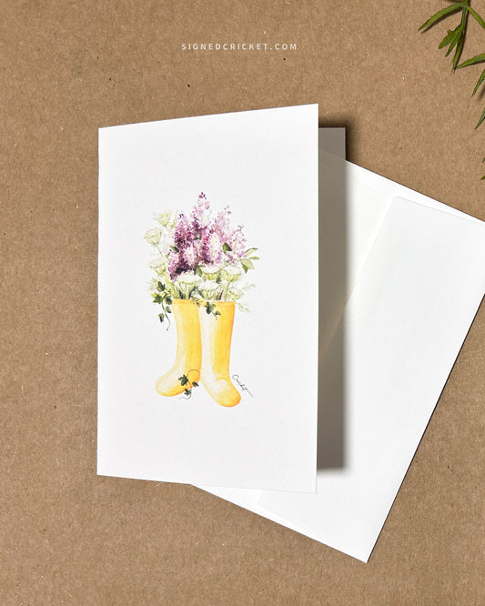 5x7 greeting card featuring watercolor illustration of yellow boots, purple liliacs, white and green Queen Anne's lace, and dark green English ivy